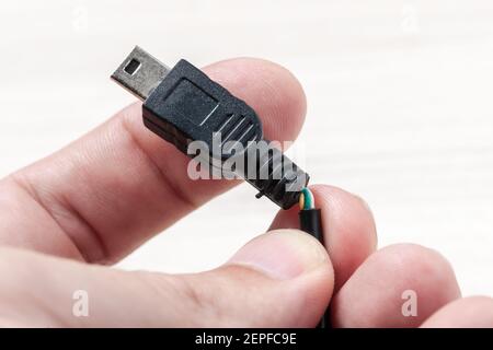 Broken black usb cable at hand on a wooden background. old wire with dust. holding broken usb transfer or charging wire. how to repair broken wires Stock Photo