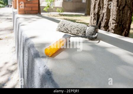 person painting outdoors with paint roller tool. paint for renovation cement garden fence Stock Photo