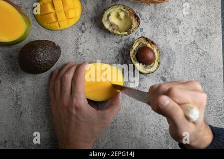 Male hands cutting mango into the cubes on marble surface Stock Photo