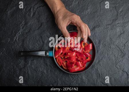 Male hand taking sliced red bell peppers from black background Stock Photo