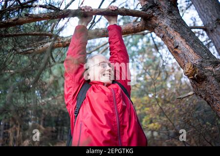 Active senior woman happy hanging from tree in the forest Stock Photo