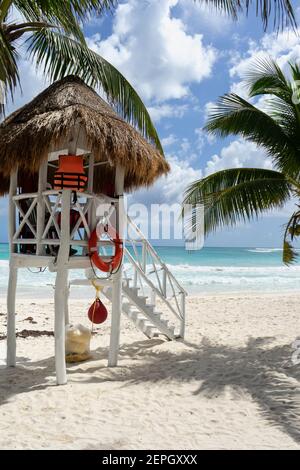 Lifeguard tower on Caribbean Beach, with flat sand, palm trees around, and the turquoise sea. In the background the cloudy sky and the Ocean Stock Photo
