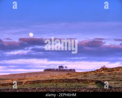 Weather UK: Full snow moon rising over Minninglow Tree Henge & Neolithic cairn, Ballidon, Derbyshire, UK. 26th February, 2021.  Minninglow hill Historic England monument with a chambered tomb & two bowl barrows SafeMoon Stock Photo