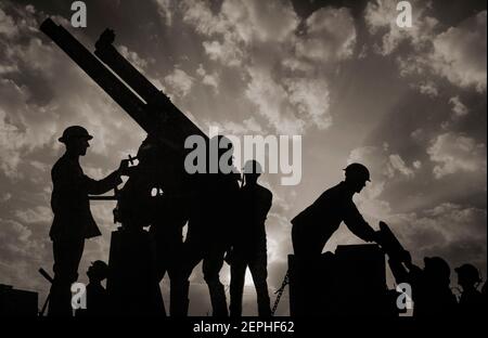 Soldiers silhouetted against the sky, are preparing to fire an anti-aircraft gun. On the right of the photograph a soldier is being handed a large shell for the gun. NB The sky has been digitally enhanced. Stock Photo