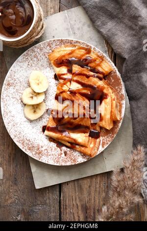 Sweet breakfast. Thin pancakes with caramel, chocolate and banana. Wooden background. Top view. Stock Photo