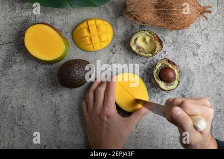 Male hands cutting mango into the cubes on marble surface Stock Photo