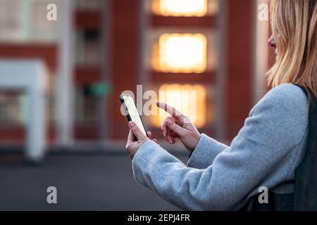Woman using her mobile phone on city street. Smartphone in female hand. Using mobile app and connecting internet outdoors Stock Photo