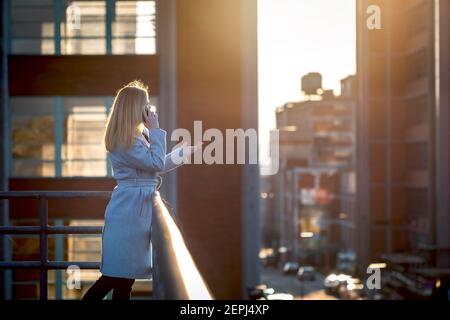 Businesswoman standing on rooftop and talking on phone. Manager woman using her smartphone. Cityscape background Stock Photo