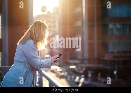 Businesswoman using her mobile phone in city. Woman holding smartphone and writing text message. Cityscape background. Stock Photo