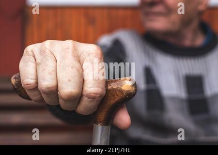 Senior man holding walking cane in his hand. Old pensioner sitting on bench and relaxing. Aging process and disability problem Stock Photo