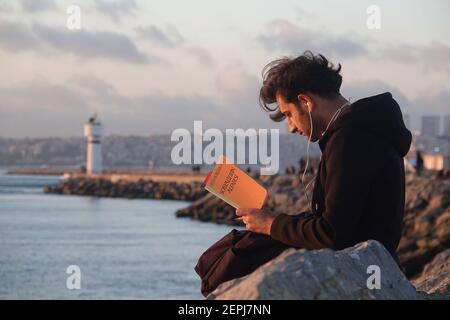 Young student reads a book on socialism at sunset, Kadikoy, Istanbul Stock Photo