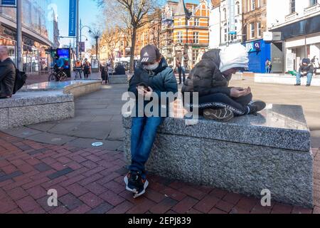 A couple of brothers sit together on a bench in the middle of Broad Street in Reading, UK. The street is relatively quiet due to.a national lockdown. Stock Photo