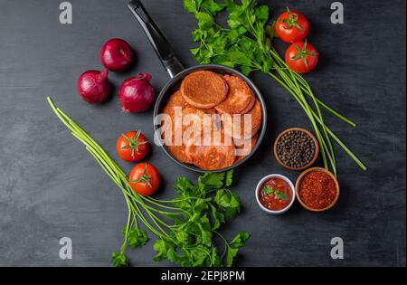 Fried salami slices in the frying pan and various kind of vegetables around Stock Photo