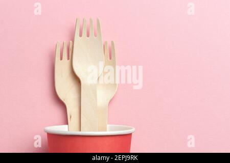 eco-friendly and disposable kitchenware. wooden forks in paper cup at pink coral background. flat lay. copy space Stock Photo