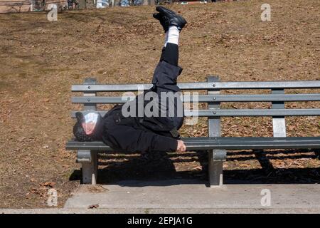 A Chinese American senior does stretching and stomach exercises while lying on a bench in Kissena Park, Flushing, New York City. Stock Photo