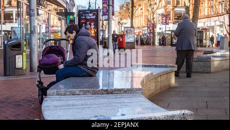 A man sits alone on marble benches with a pram in Broad Street, Reading, UK Stock Photo