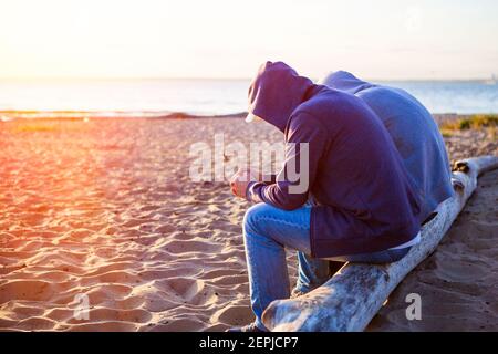 Two Sad Men sit on the Log at the Beach Stock Photo