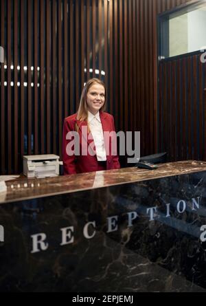 A pleasant female receptionist waiting for the guests behind the counter at the hotel. Tourism, business, hotel Stock Photo