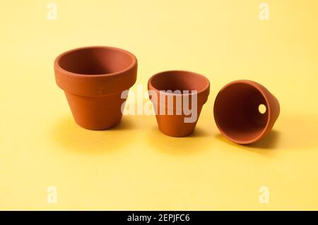 3 small but different sized clay pots stand and lie on a yellow background. With free space for text Stock Photo