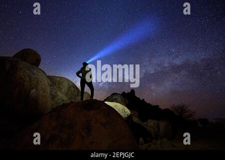 Silhouette of lone woman on rounded rocky structures gazing at milky way and the stars, focused beam of headlamp pointing directly to milky way. Night Stock Photo