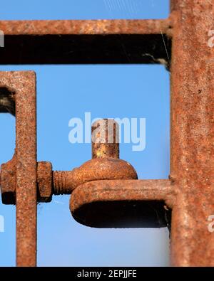 Close-up of old rusty wrought iron gate hinge seen against a blue sky Stock Photo