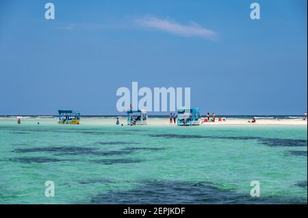 Several glass bottom boats moored by a low tide sand bank with people on the sand, Diani, Kenya Stock Photo