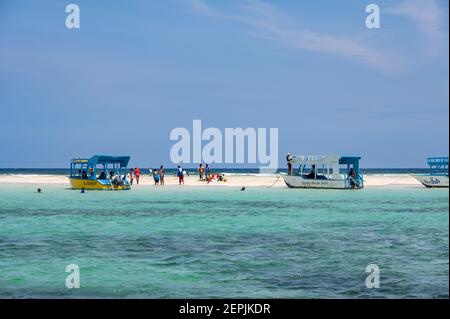 Several glass bottom boats moored by a low tide sand bank with people on the sand, Diani, Kenya Stock Photo