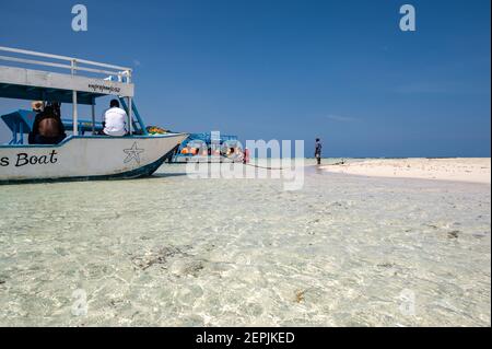A glass bottom boat moored by a low tide sand bank with people on the sand, Diani, Kenya Stock Photo