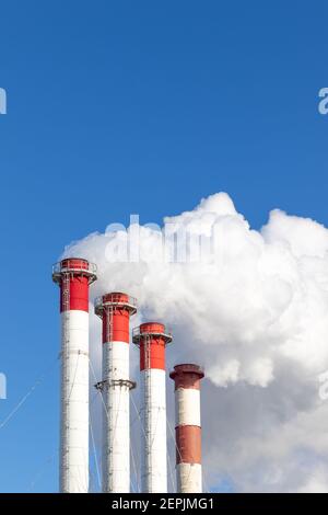 red-white chimneys of the boiler room, equipped with a traffic light. white smoke against blue sky on sunny frosty winter day Stock Photo