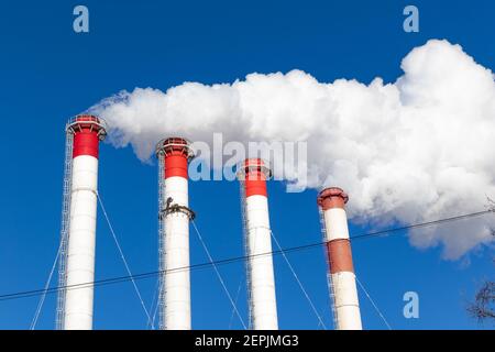 red-white chimneys of the boiler room, equipped with a traffic light. white smoke against blue sky on sunny frosty winter day Stock Photo