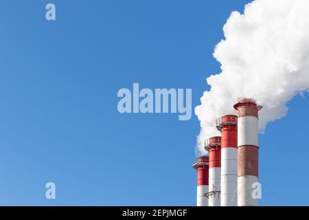 red-white chimneys of the boiler room, equipped with a traffic light. white smoke against blue sky on sunny frosty winter day Stock Photo