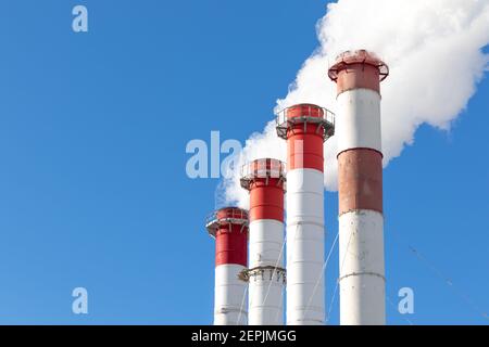 red-white chimneys of the boiler room, equipped with a traffic light. white smoke against blue sky on sunny frosty winter day Stock Photo