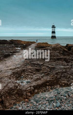 Coastal path leading to a young lady on her back looking to a lighthouse in a cold atmosphere Stock Photo