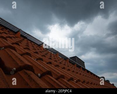 Dramatic thunderstorm clouds above a red tiled roof with a chimney, dark sky in background Stock Photo