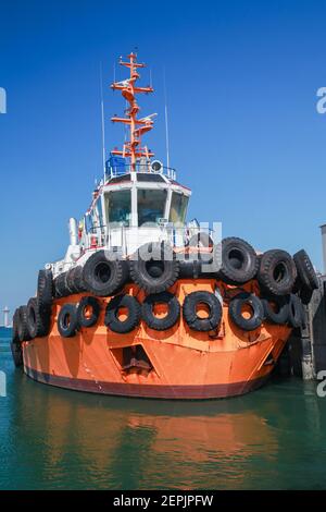 Tug boat with  bright orange hull is moored in a port of Saudi Arabia. Vertical photo Stock Photo