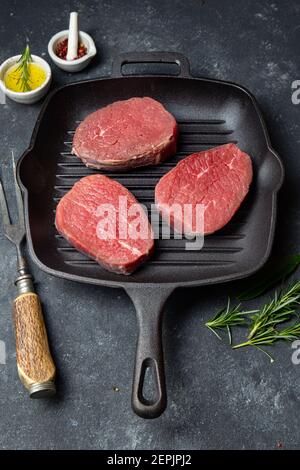 Raw beef steaks on cast iron grill pan. Top view, black background Stock Photo