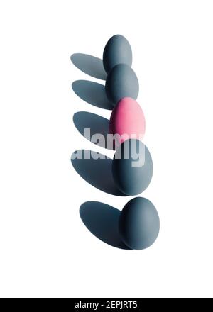 five eggs stand in a row against a white background. One stands out in pink color Stock Photo