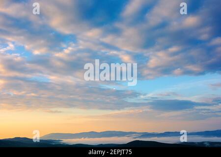 cloudscape in summer at sunrise. clouds on the blue sky in yellow and pink morning light. idyllic weather condition, picturesque scenery above the mou Stock Photo
