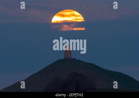 Glastonbury, Somerset, UK.  27th February 2021.  UK Weather.  The full snow moon rises up from behind a layer of cloud at Glastonbury Tor in Somerset at dusk.  Picture Credit: Graham Hunt/Ģ����ý Live News Stock Photo