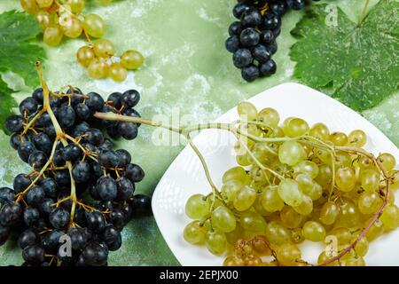 A plate of white grapes and black grapes with leaves on green ...