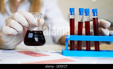 Hand of a scientific taking a blood sample tube from stand. Woman working with blood samples in laboratory, closeup Stock Photo