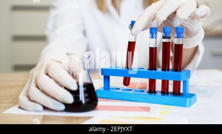 Hand of a scientific taking a blood sample tube from stand. Woman working with blood samples in laboratory, closeup Stock Photo