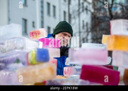 Man participating in a community project of building an ice castle or fortress from colored ice bricks or blocks in Munkkiniemi, Helsinki, Finland Stock Photo
