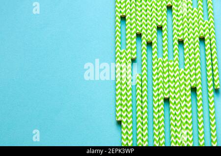 disposable green and white straws are laid out on a background of blue paper Stock Photo