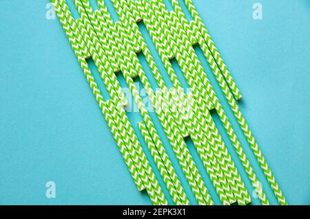 disposable green and white straws are laid out on a background of blue paper Stock Photo
