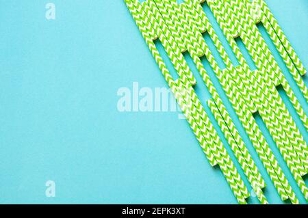 disposable green and white straws are laid out on a background of blue paper Stock Photo