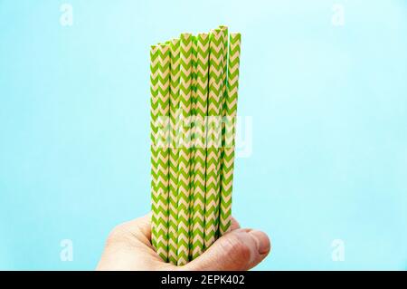 disposable green-white straws are located in the hands against a blue background Stock Photo