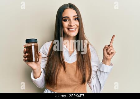 Beautiful brunette young woman holding soluble coffee smiling happy pointing with hand and finger to the side Stock Photo