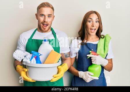 Young couple of girlfriend and boyfriend wearing apron holding products and cleaning spray celebrating crazy and amazed for success with open eyes scr Stock Photo