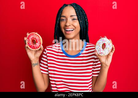 Beautiful hispanic woman holding tasty colorful doughnuts smiling and laughing hard out loud because funny crazy joke. Stock Photo